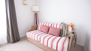 A modern bedroom with a striped sofa bed, a floor lamp, and a large window with curtains.