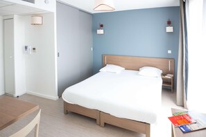 A hotel room with a bed, bedside table, lamp, and a view of the outside.