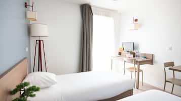 A hotel room with two beds, a desk with a chair, a TV, a lamp, and a potted plant.
