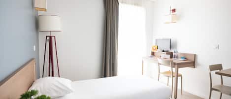 Habitación de hotel con dos camas, un escritorio con silla, televisión, lámpara y planta en maceta.