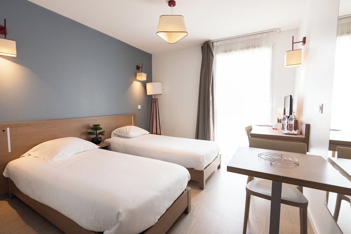 Een hotelkamer met twee bedden, een bureau, een stoel, een lamp en een klein tafeltje met een dienblad.