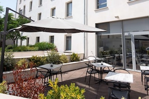 An outdoor patio with tables and chairs, a large umbrella, and a building in the background.