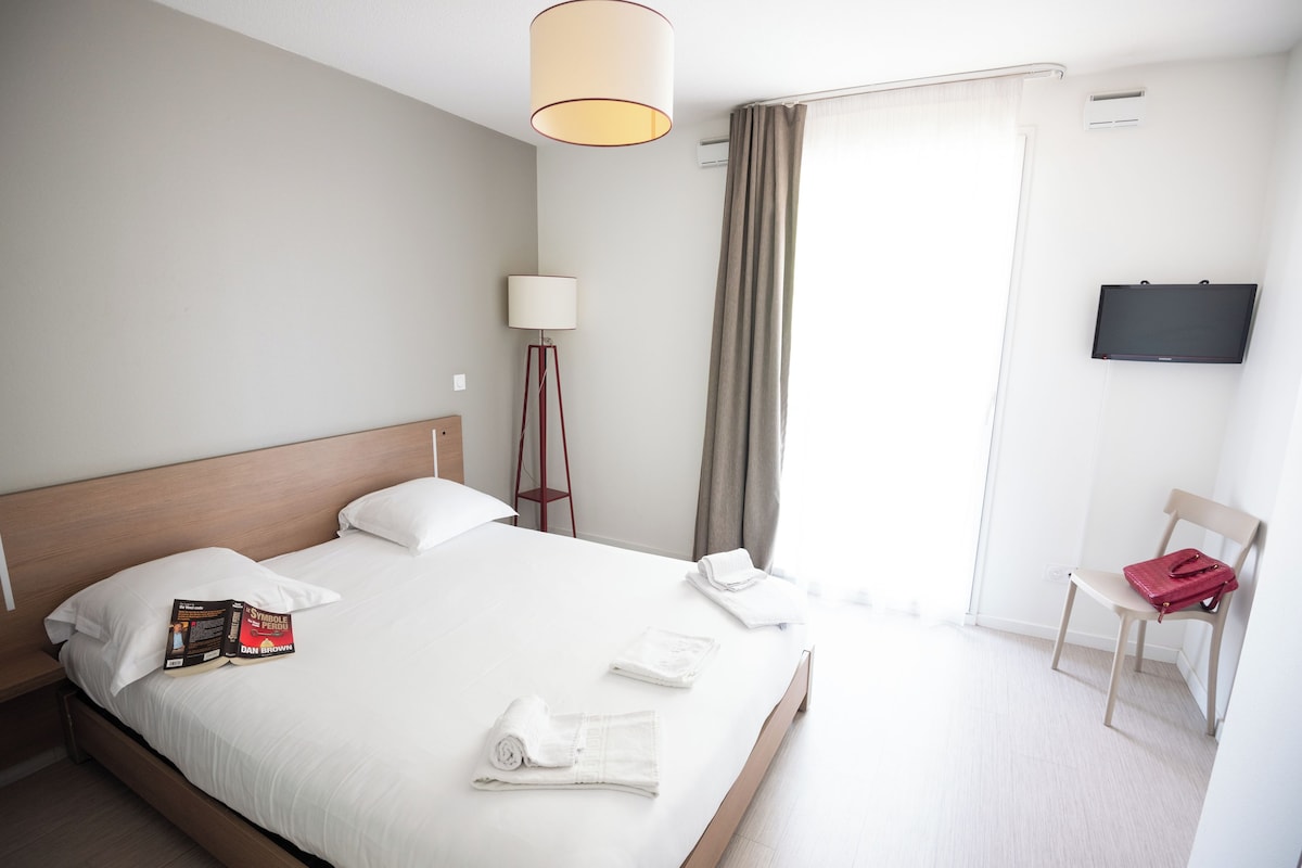 Une chambre d’hôtel avec un lit bien fait, une lampe de chevet, une chaise et un téléviseur fixé au mur.