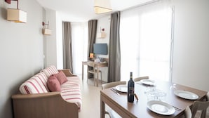 A modern hotel room with a sofa, dining table, and a TV. - Zenitude Hotel-residences Narbonne (Narbonne)