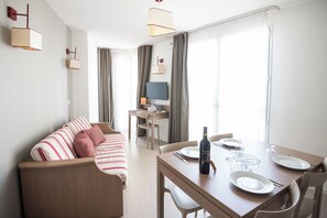 Una habitación de hotel moderna con sofá, mesa de comedor y televisor.