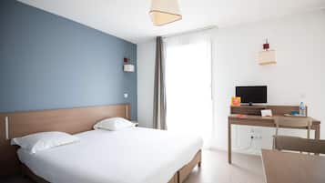 A hotel room with a bed, desk, chair, television, and curtains.