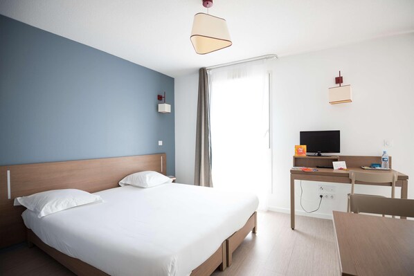 Una habitación de hotel con cama, escritorio, silla, televisor y cortinas.
