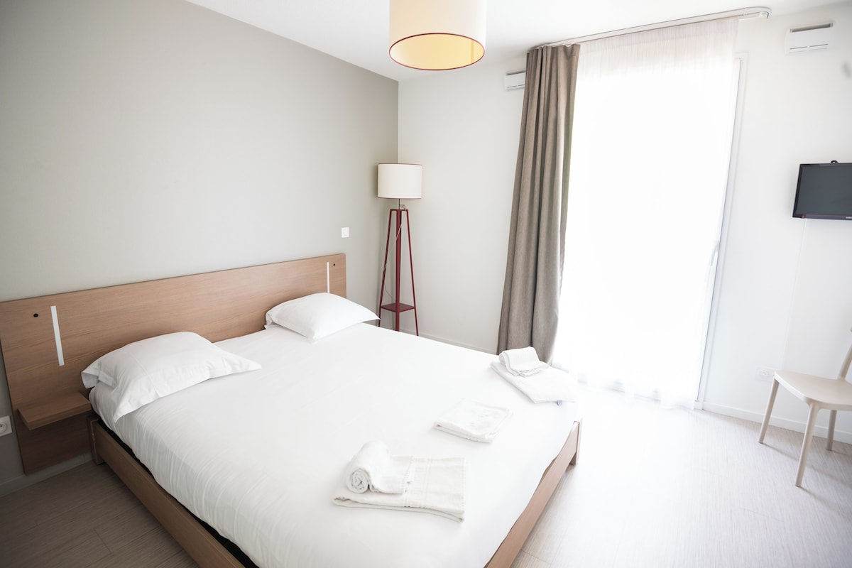 Een moderne hotelkamer met een groot bed, een nachtkastje, een lamp, een stoel en een televisie aan de muur.