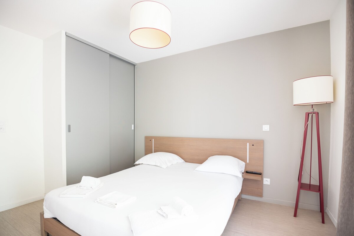 Et moderne soveværelse med en træseng, hvide sengetøj, et natbord, en gulvlampe og et garderobeskab.