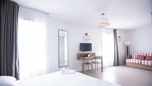 A hotel room with a large bed, a desk with a TV, and a sofa.
