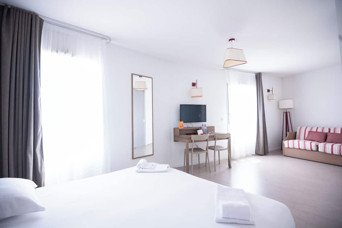 A hotel room with a large bed, a desk with a TV, and a sofa.