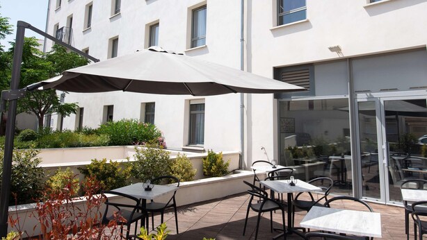 An outdoor patio with tables and chairs, a large umbrella, and a building in the background.