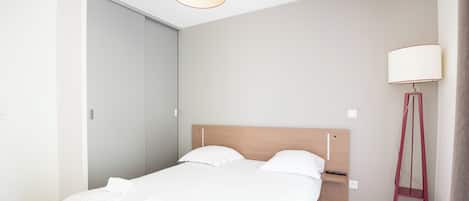 Un dormitorio moderno con una cama de madera, ropa de cama blanca, una mesita de noche, una lámpara de pie y un armario.