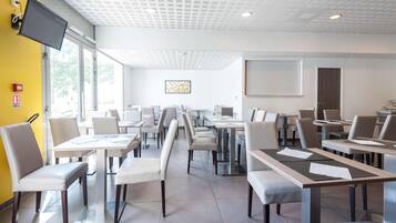 A modern conference room with tables and chairs, a flat-screen TV, and a large window.