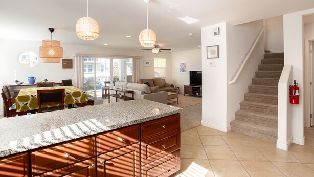 A spacious kitchen with a granite countertop, wooden cabinets, and pendant lighting. A dining area with a table and chairs is visible in the background.