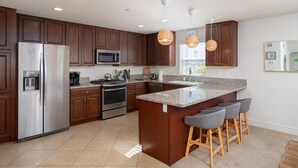 A modern kitchen with dark wood cabinets, stainless steel appliances, a granite countertop, and a central island with bar stools.