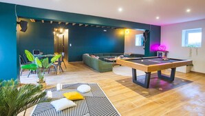 A modern living room with a pool table, a sofa, and a dining area with chairs and a table.