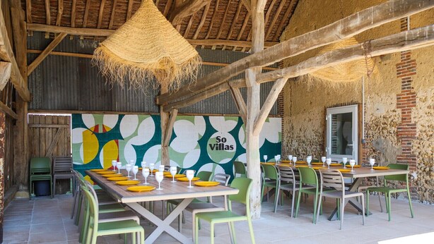 An outdoor dining area with tables set for two, surrounded by green chairs.