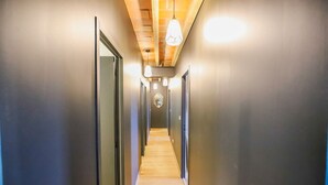 A long, narrow hallway with wooden flooring and dark walls, leading to a door at the end.