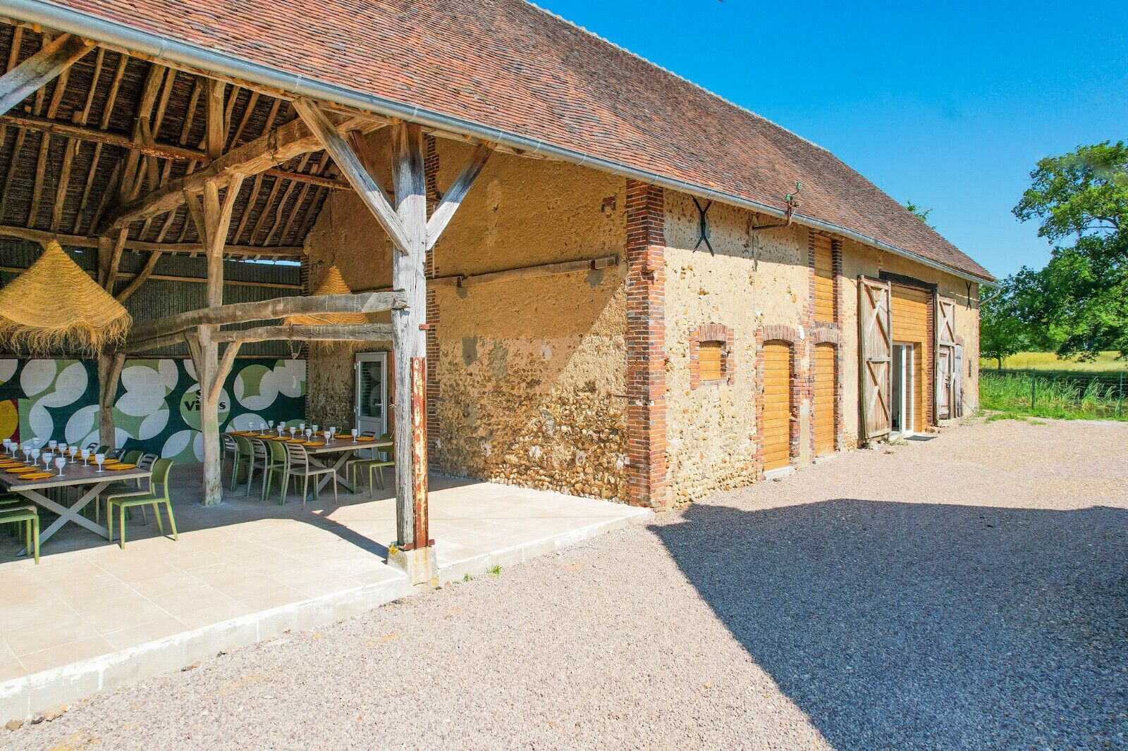 A rustic building with a thatched roof and stone walls, featuring outdoor seating and a gravel ground.