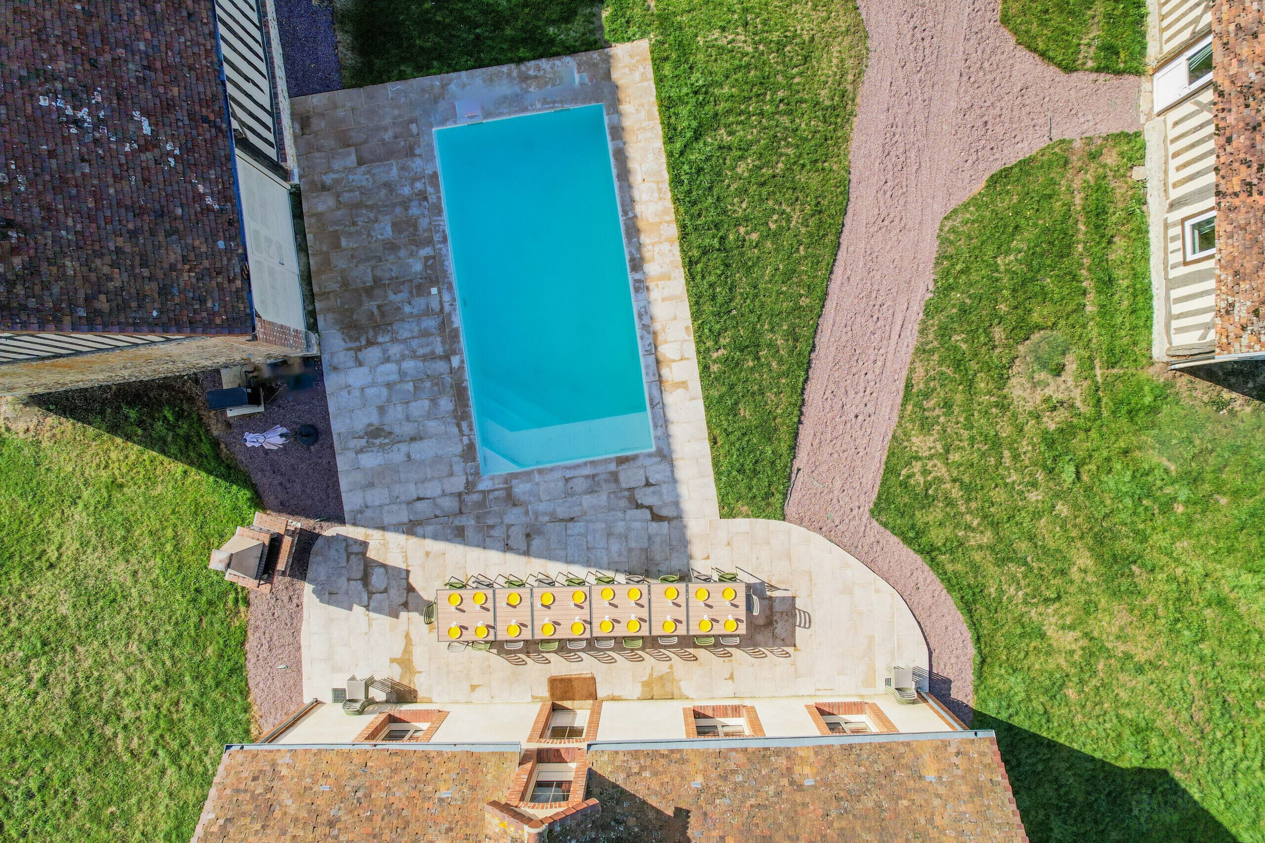 An aerial view of a property with a swimming pool, a patio area with seating, and a brick building.