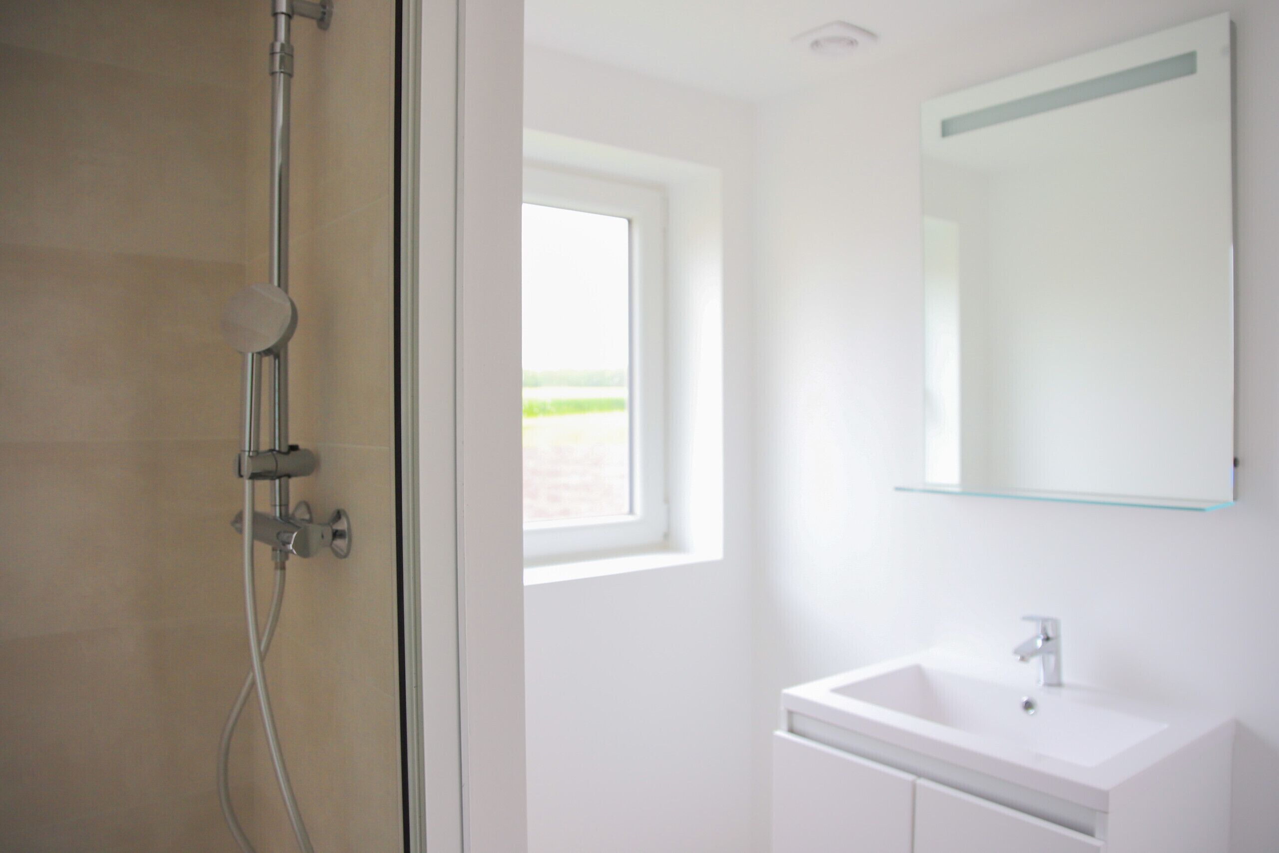 A bathroom with a shower, a sink, and a window.