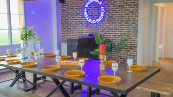 Una mesa de comedor con platos amarillos y copas de vino, una vela y un letrero de neón en una pared de ladrillo.