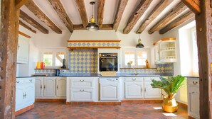 A spacious kitchen with white cabinets, a tiled backsplash, and a brick floor.