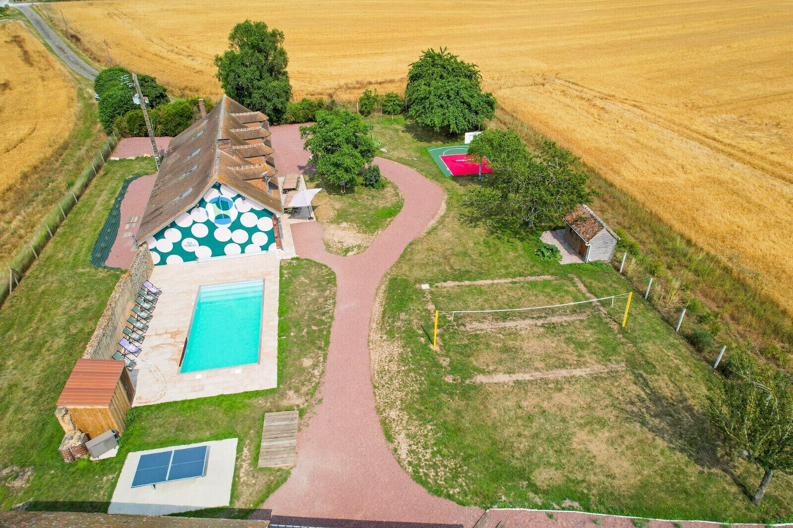 Vista aérea de una propiedad con piscina, cancha de tenis y un edificio pequeño.