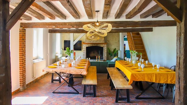 A dining area with a brick fireplace, wooden beams, and a staircase leading to an upper level.