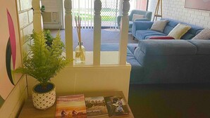 Un salon avec un canapé bleu, une plante en pot et une fenêtre avec des stores.