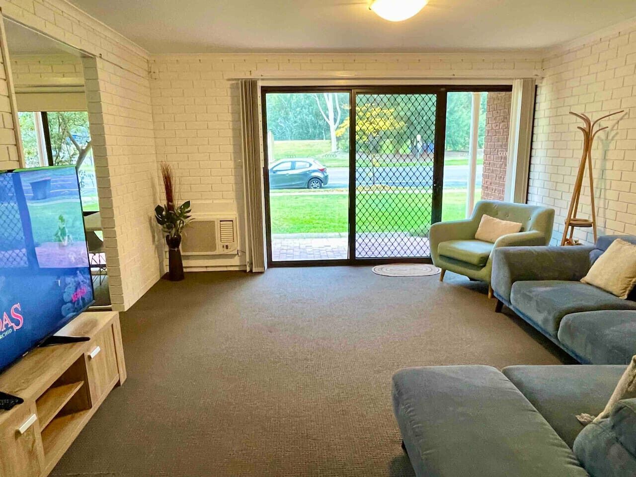 Ein Wohnzimmer mit Fernseher, Sofas, einer Schiebetür und einer Ziegelwand.