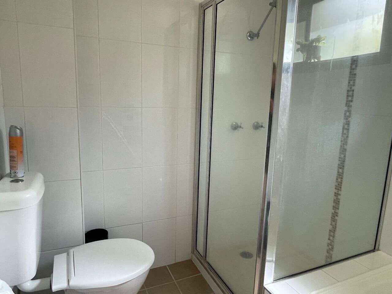 Un bany amb un vàter, una cabina de dutxa amb vidre i parets de rajola blanca.