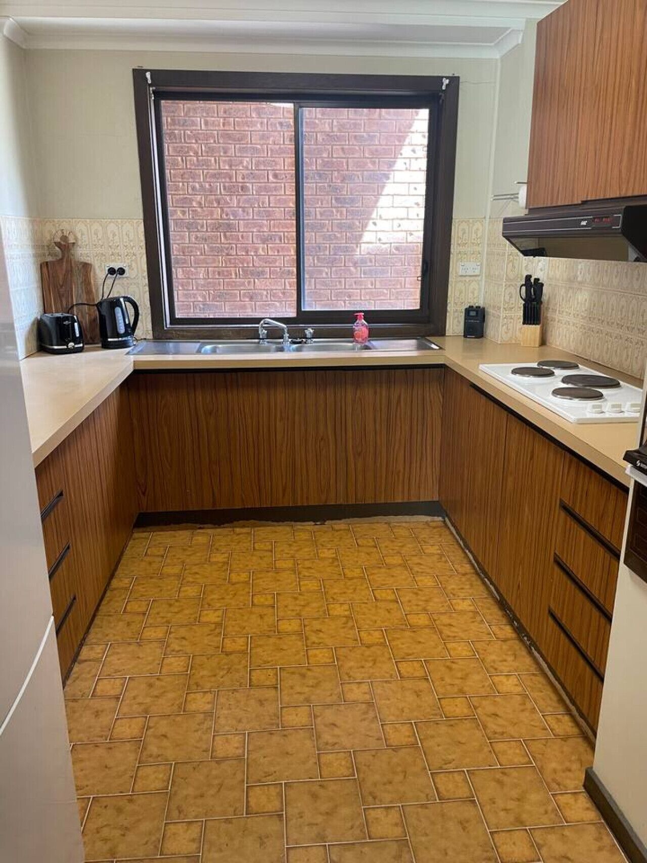 A kitchen with a window, a sink, a stove, and wooden cabinets.