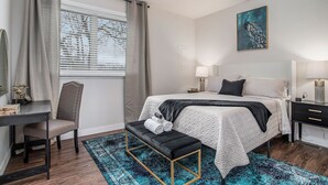 Une chambre à coucher comprenant un lit, des tables de chevet, un bureau, une chaise, un banc et un ventilateur de plafond.