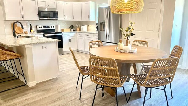A modern kitchen with white cabinets, a central island, and a dining area with wicker chairs.