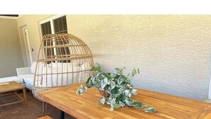 A wooden table with benches, a wicker chair, and a potted plant with variegated leaves.