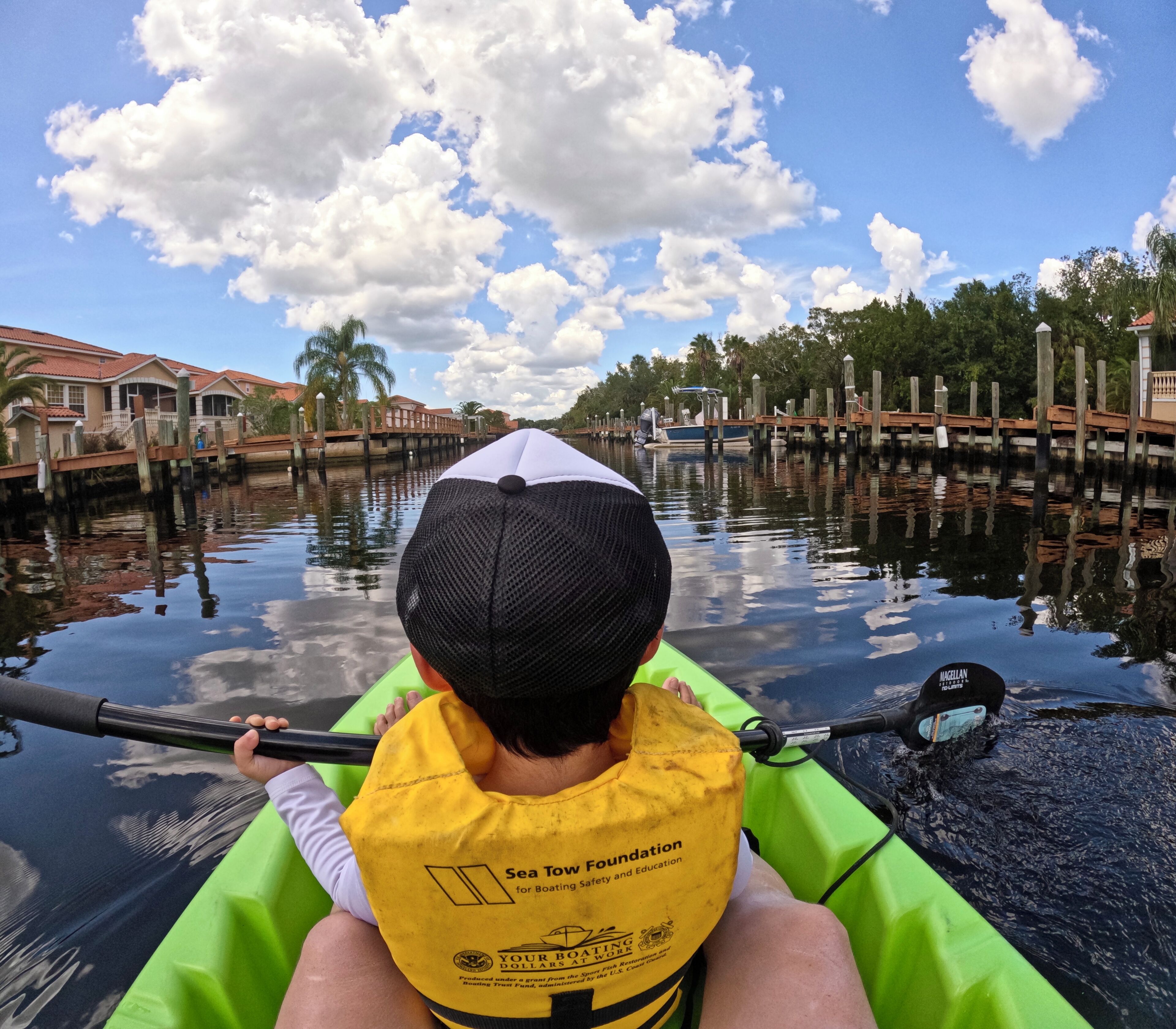 A person in a kayak on a calm waterway with wooden docks and houses in the background.