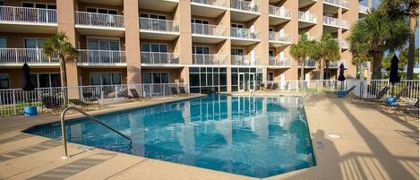 A hotel with a swimming pool, multiple balconies, and palm trees.