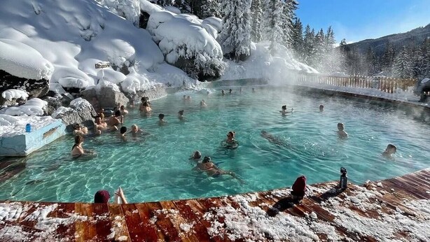Uma fonte termal natural rodeada por árvores e rochas cobertas de neve.