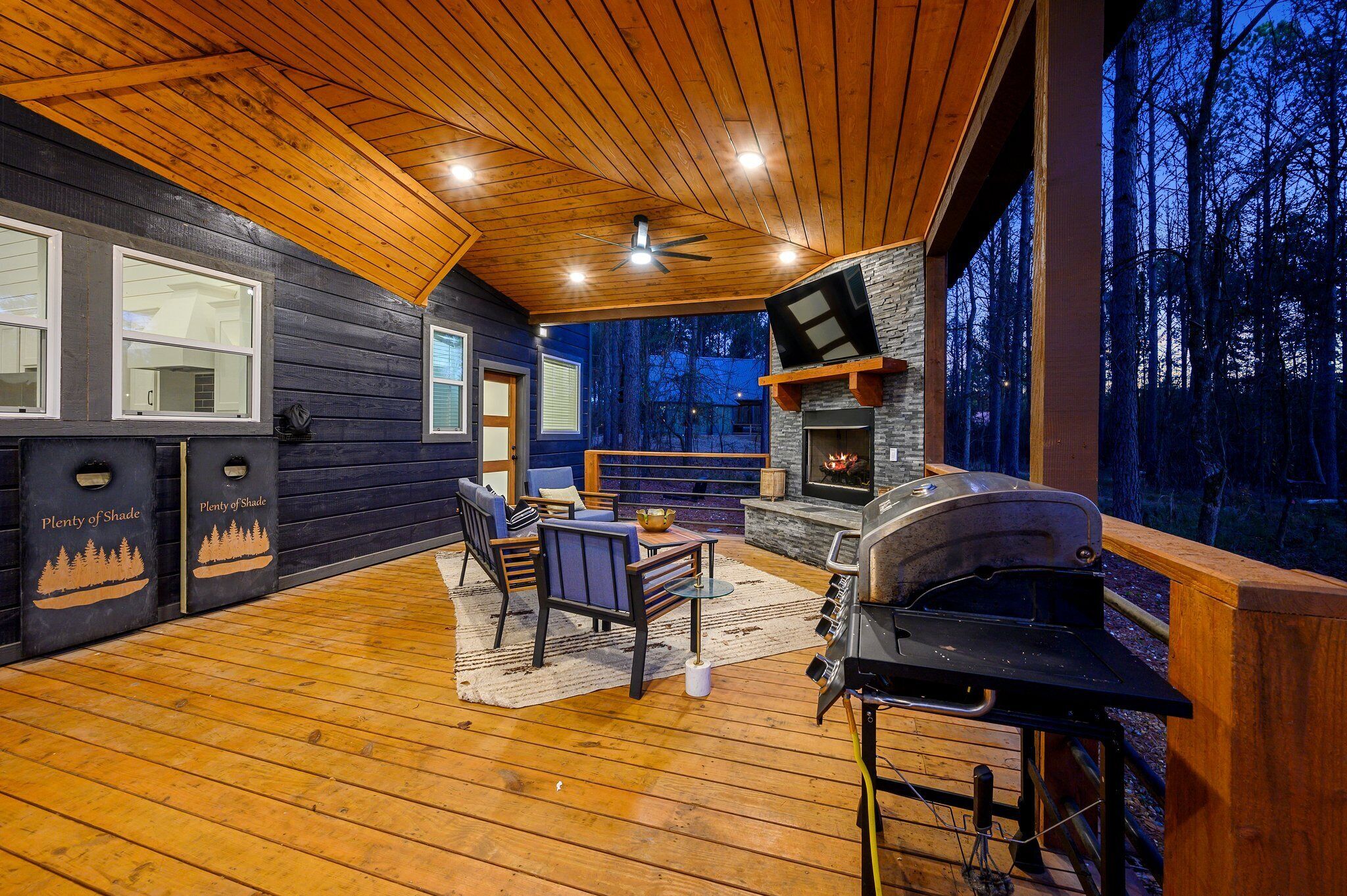 A wooden deck with a stone fireplace, outdoor seating, and a TV mounted on the wall.