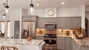 Una cocina moderna con gabinetes grises, electrodomésticos de acero inoxidable, encimera de mármol e iluminación colgante.
