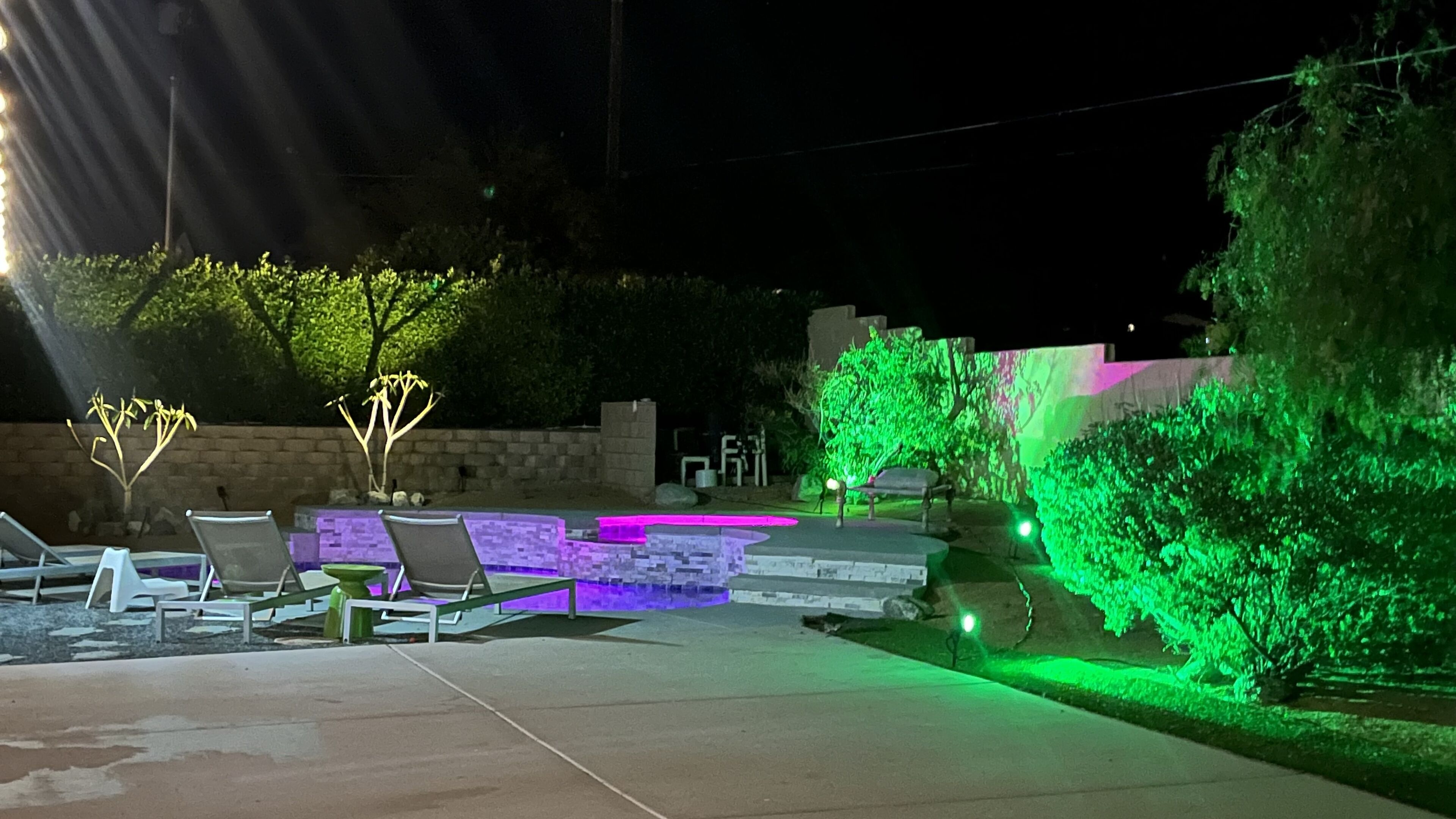 Un espace extérieur aménagé pour la nuit, avec une piscine, des chaises longues et des arbres illuminés.