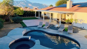 Un patio trasero con piscina, mobiliario de exterior y una zona de estar cubierta.