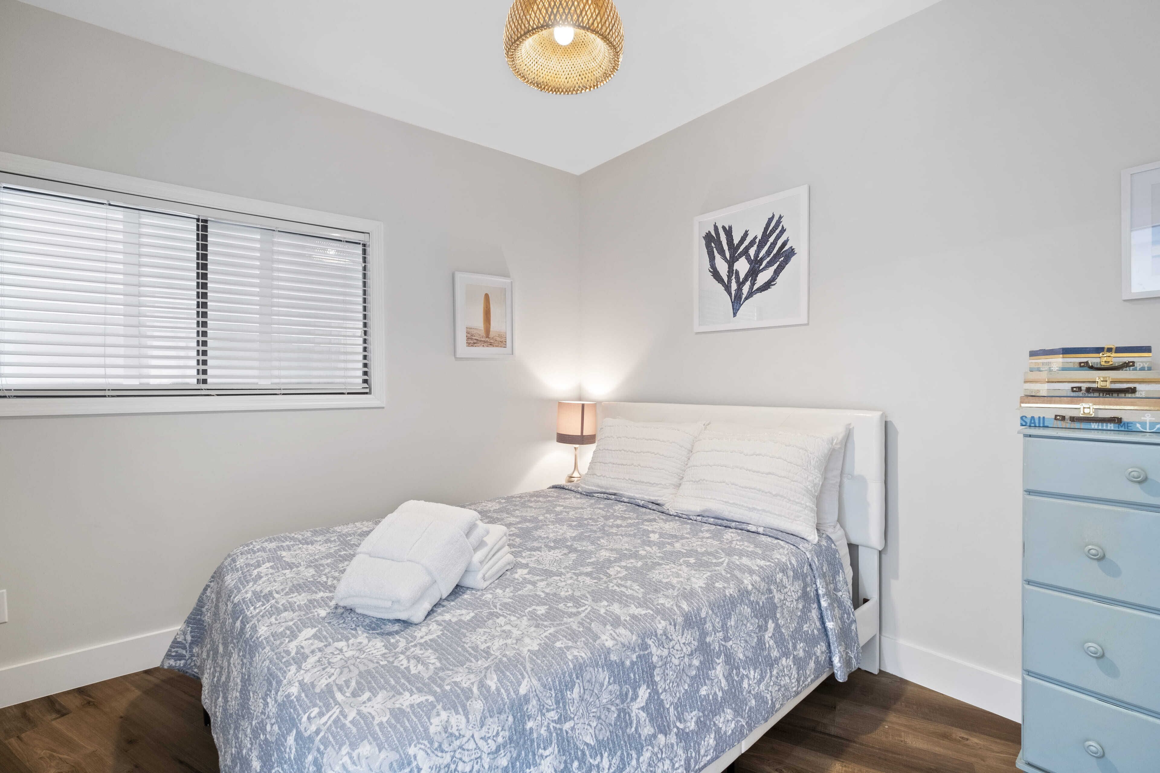 A bedroom with a bed, a bedside lamp, a window with blinds, and a dresser.