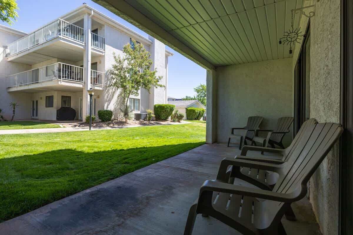 Un espace extérieur abrité, doté d’un sol en béton, d’une rangée de fauteuils Adirondack et, au fond, d’un bâtiment à deux étages.