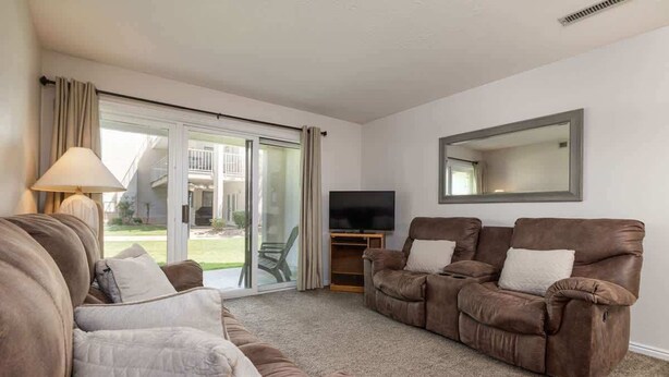 Una sala de estar con un sofá, dos sillones, un televisor y un ventanal corredizo que da a un patio.
