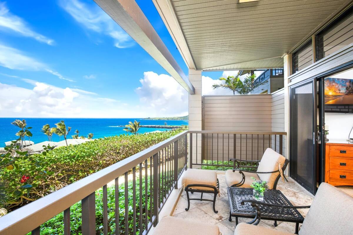 A balcony with a view of the ocean, outdoor furniture, and a sliding glass door.