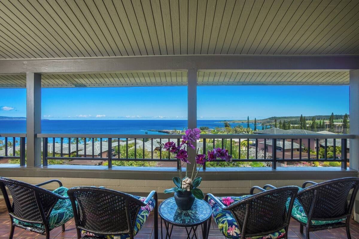 A covered outdoor seating area with a view of the ocean and a distant landscape.