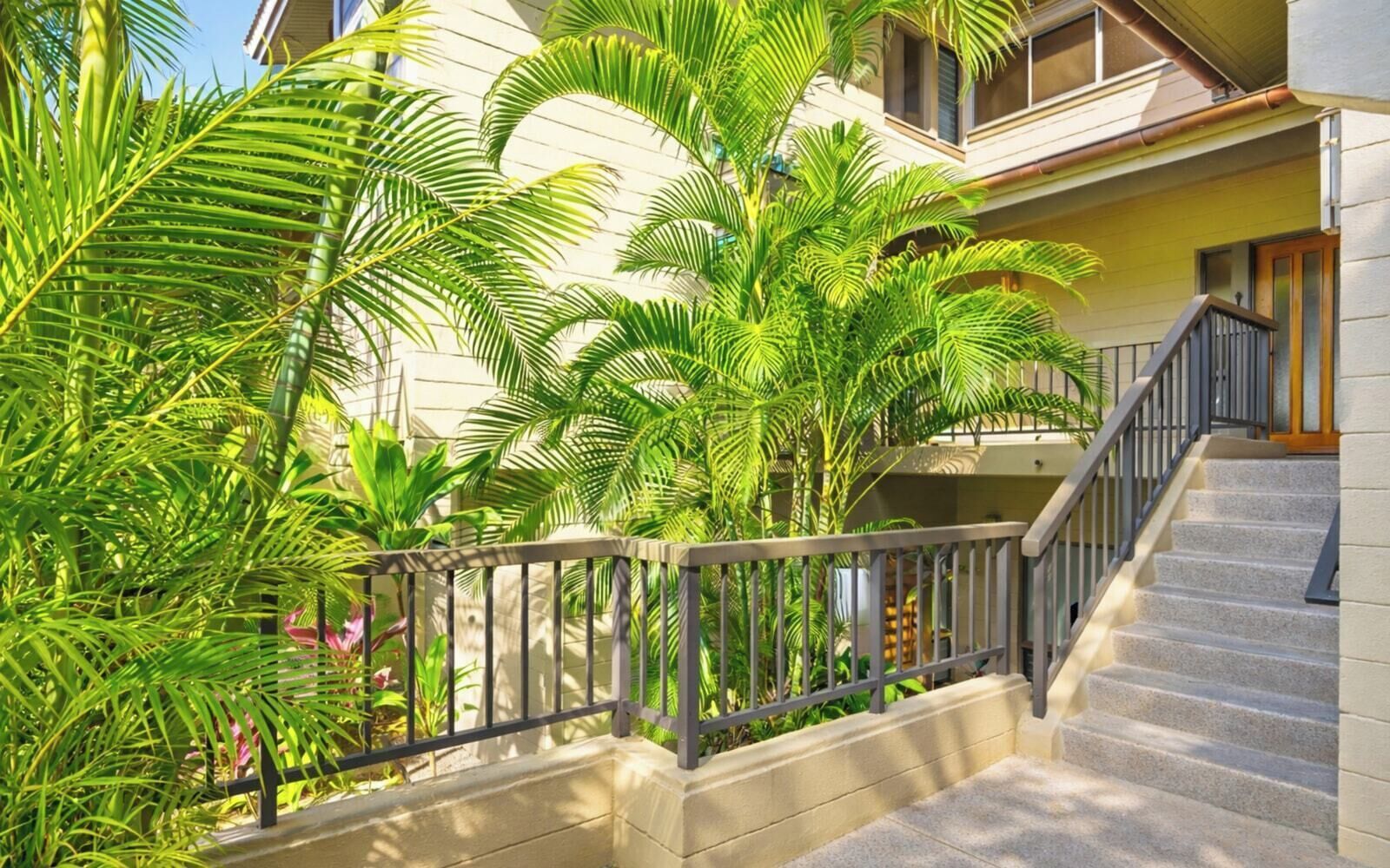 A residential building with a staircase, palm trees, and a balcony.
